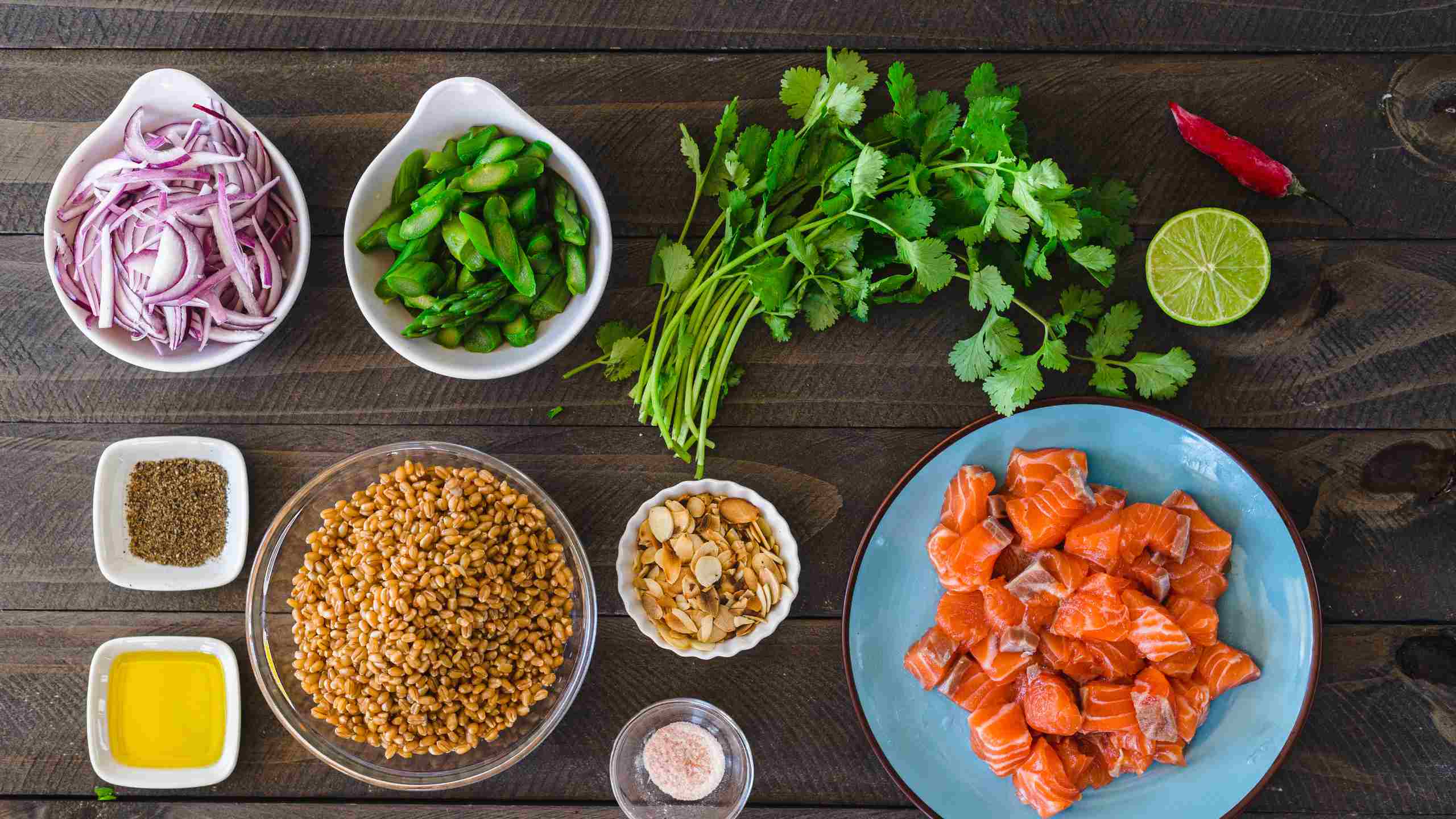 Alimentos para confecionar receita separados em taças: salmão em cubos, cebola, espargos, amêndoas laminadas.