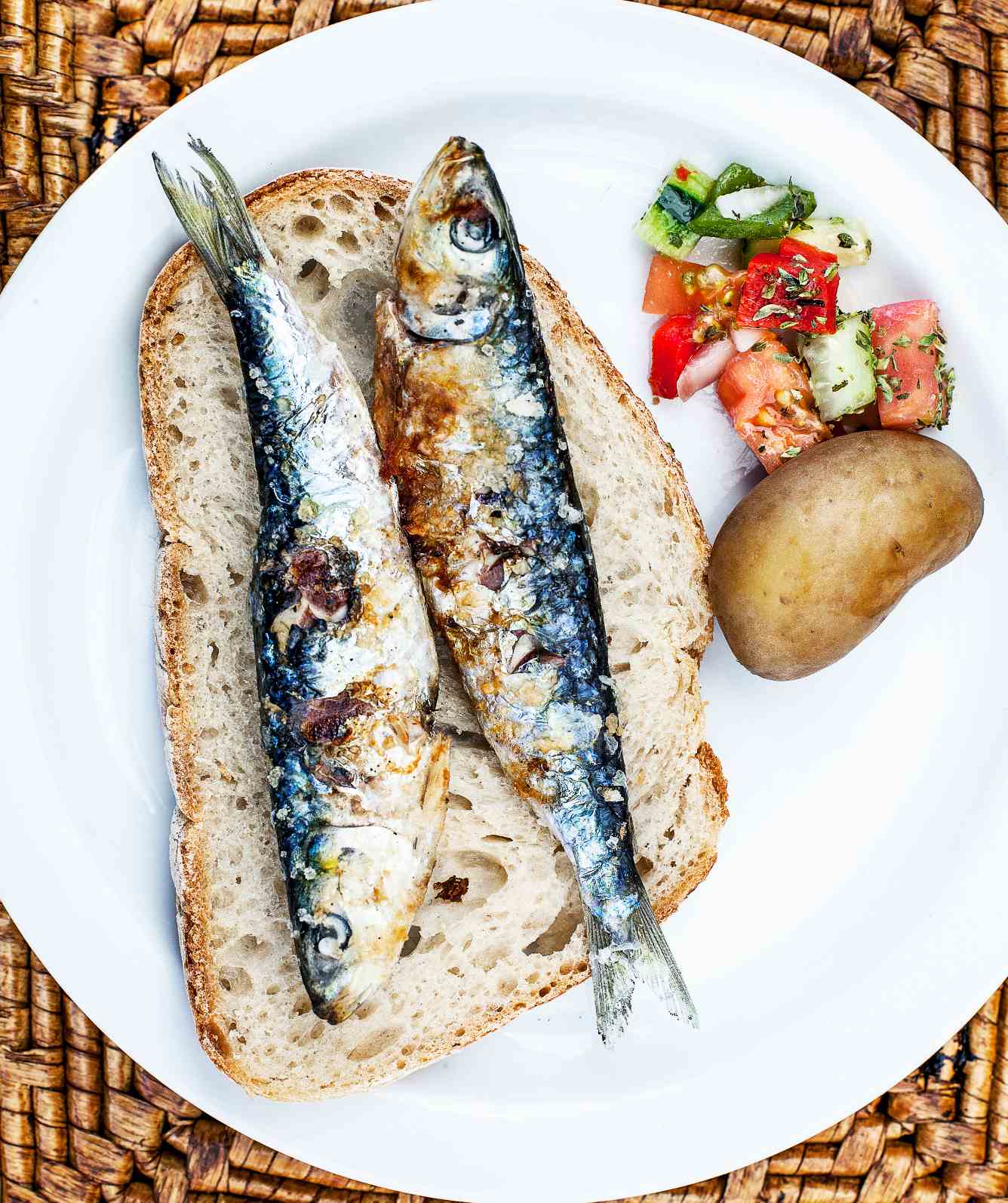 Two sardines on a slice of bread, with potato and salad, in a ceramic plate.