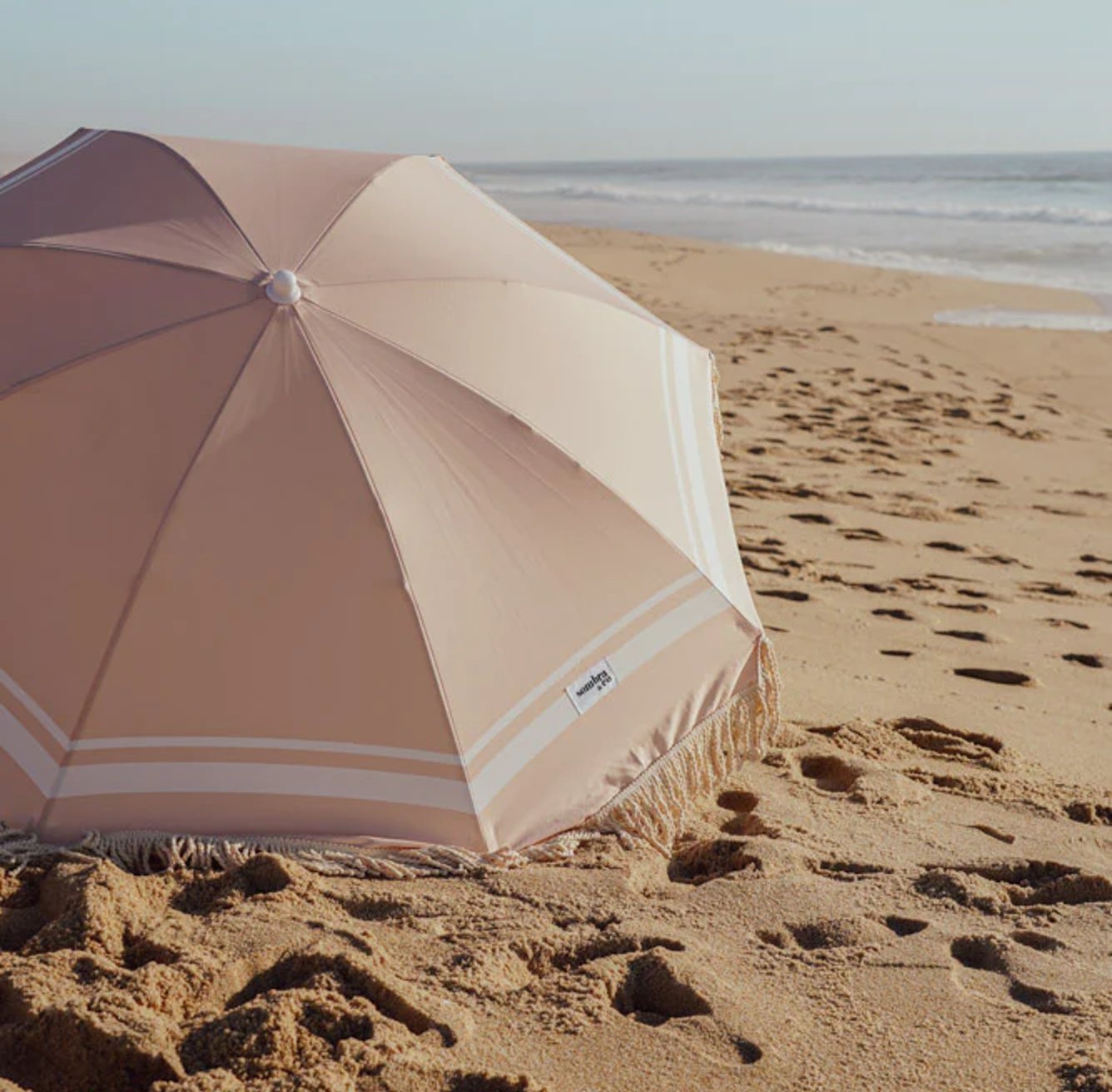 Sombra & Co beach umbrella laid on the sand.