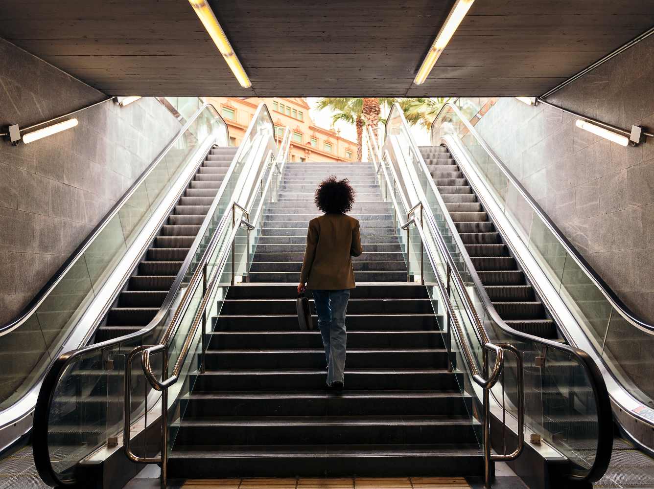 Mulher subindo escadas a pé, ao lado de escadas rolantes.