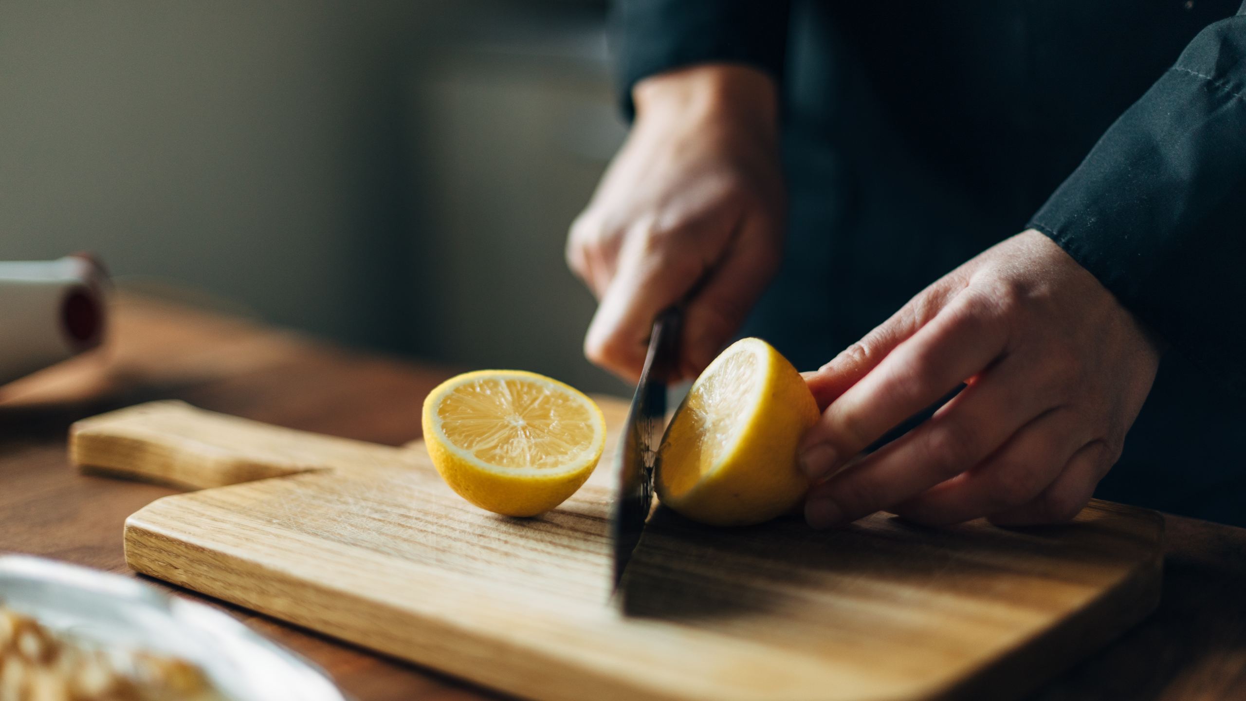 Hands slicing a lemon in half, on a wooden cutting board.