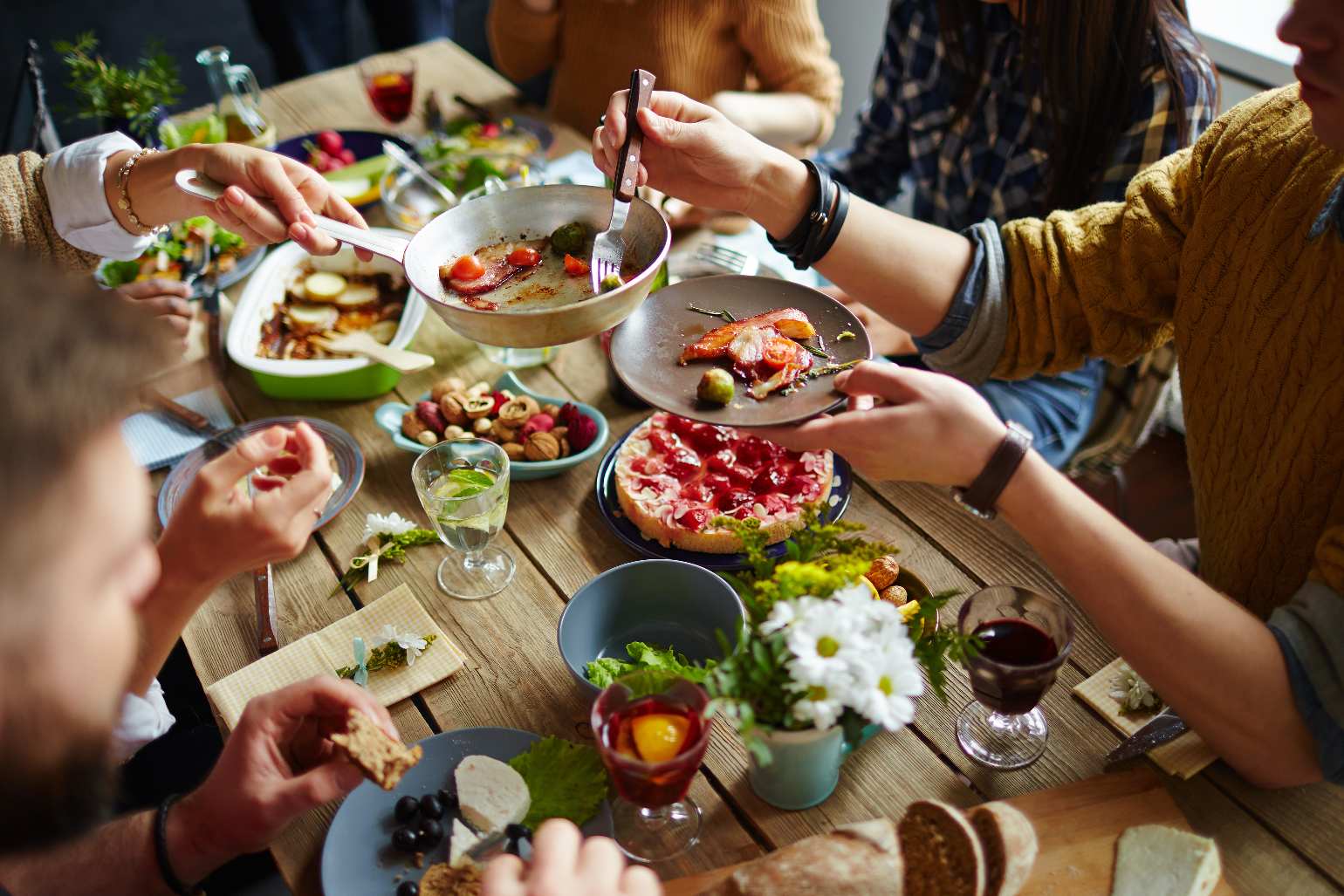 Mesa servida com vários pratos, e mãos de pessoas partilhando a refeição.