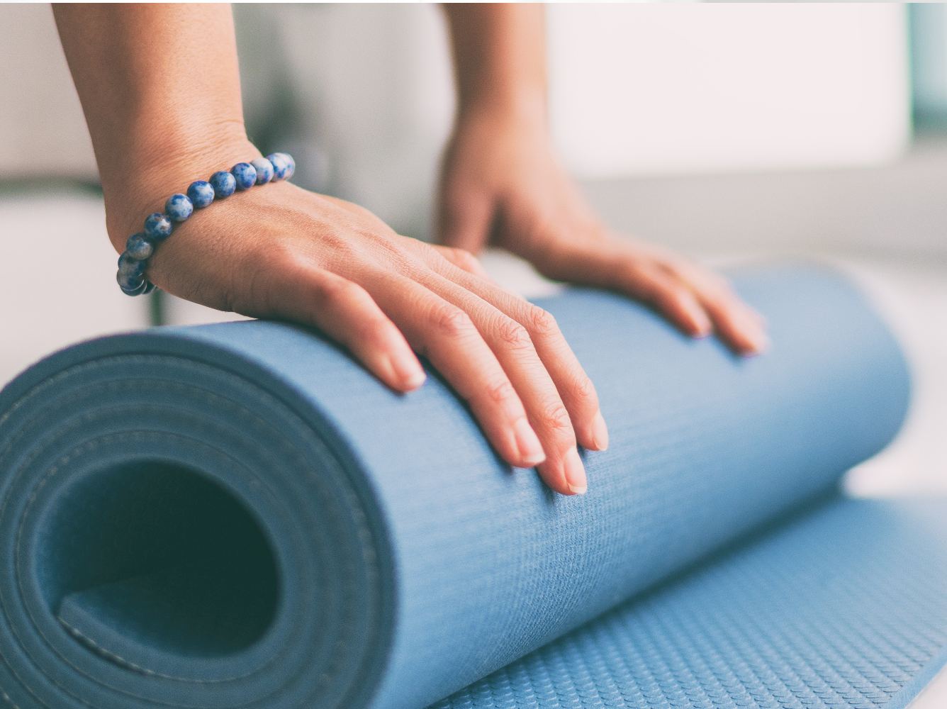 Mãos femininas desenrolando tapete de yoga.