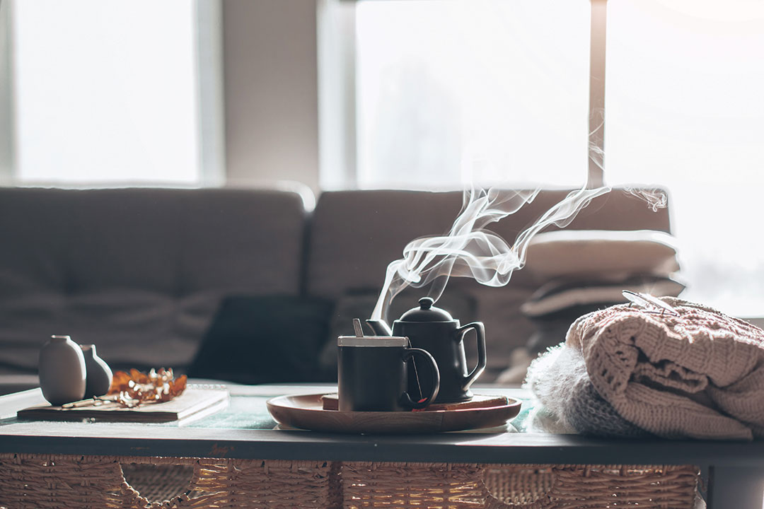 Still life details in home interior of living room. Sweaters and cup of tea with steam on a serving tray on a coffee table.