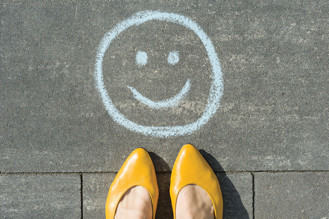 Symbol of happy smiley drawn on the asphalt and woman feet.