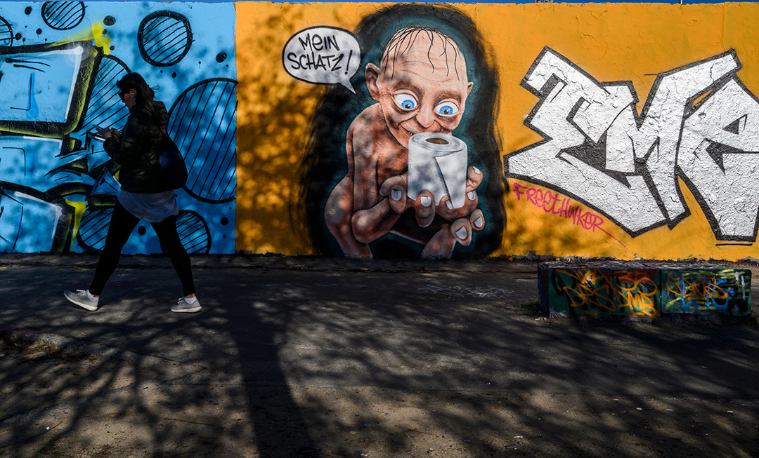 A woman walks past a mural painting by graffiti artist Eme Freethinker depicting a likeness of the Gollum/Smeagol of the "Lord of the Rings" epic, worhsipping a toilet paper roll with a speech bubble reading "My darling", at Berlin's Mauer Park on March 21, 2020, amidst the new coronavirus COVID-19 pandemic.