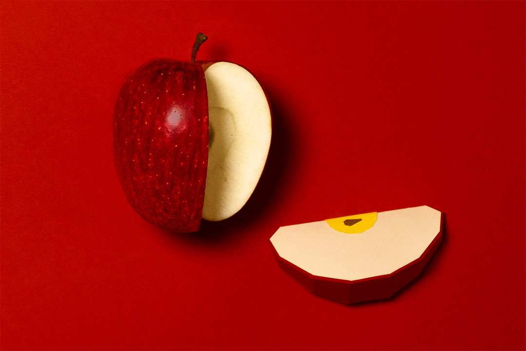 a real apple and a apple slice made of paper, on red background