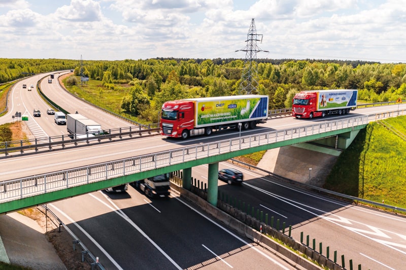  aerial image of two biedronka trucks on a bridge, crossing it, on a clear day.  
