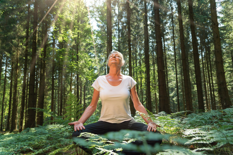 woman sitted on the ground in a green forest, with eyes closed