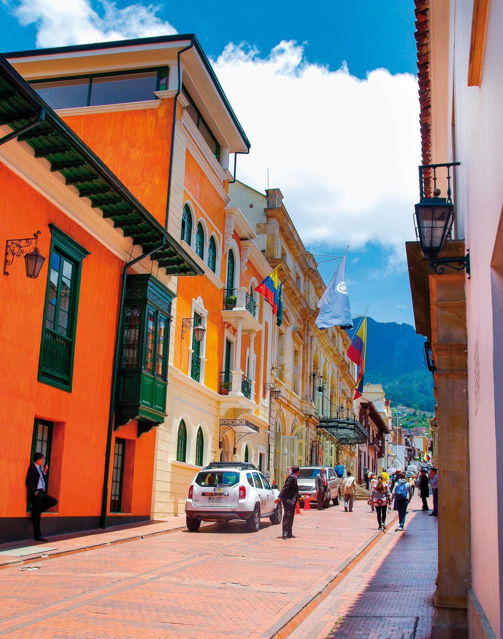 photo of a street with colorful buildings and green mountains in the back, in bogotá, colombia