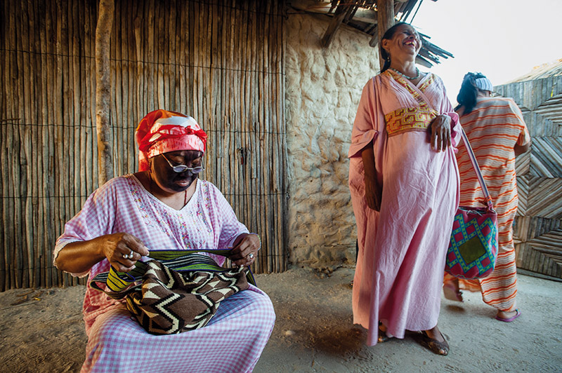 one colombian women sitted and grabbing a wayuu bag, while another woman stands beside her, laughing