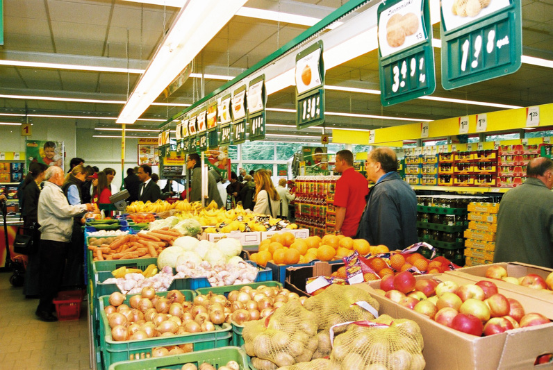 Old photo of the inside of the first biedronka store, with customers shopping on the fruis and vegetables corridor