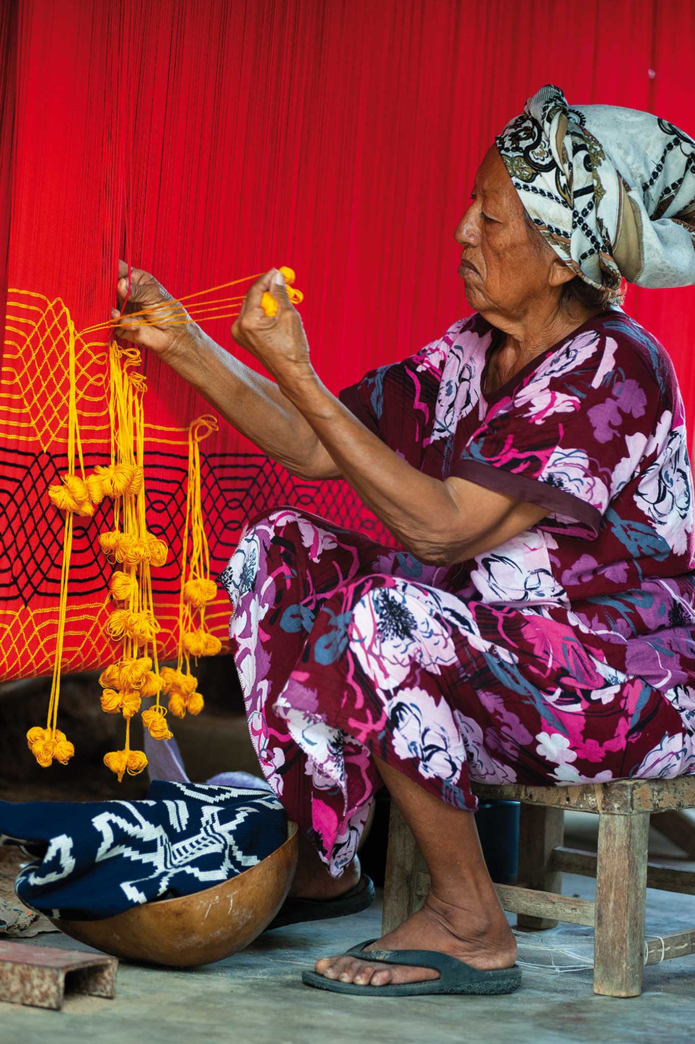 elderly woman, sitting on a chair and weaving a wayuu bag