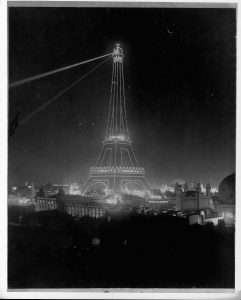 Spotlights illuminate the Eiffel Tower at night during the 1900 Exposition.