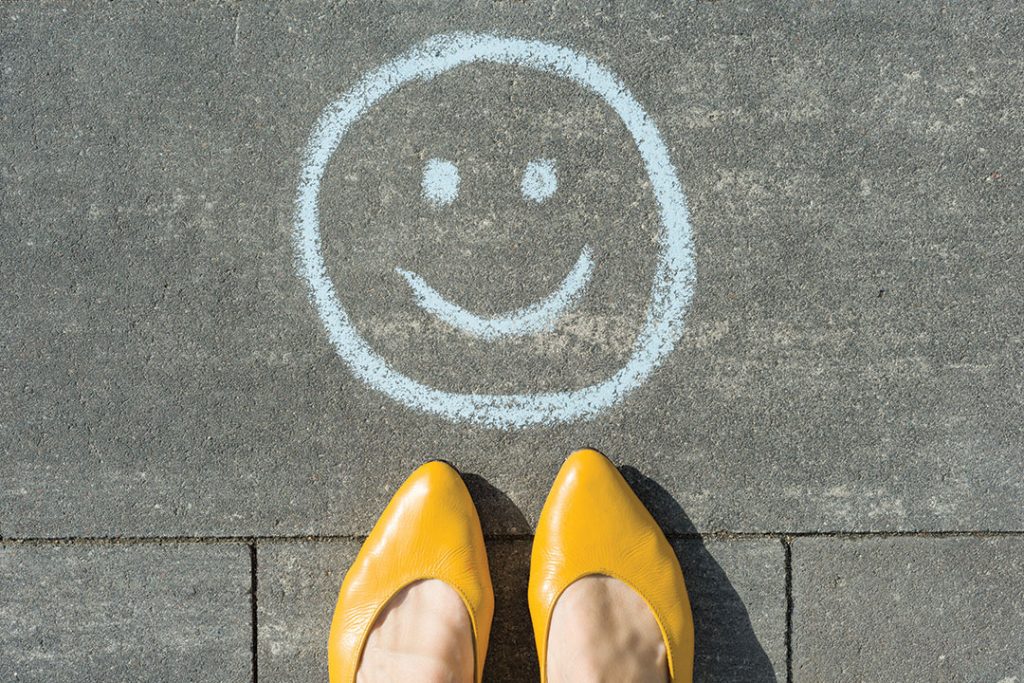 Symbol of happy smiley drawn on the asphalt and woman feet.