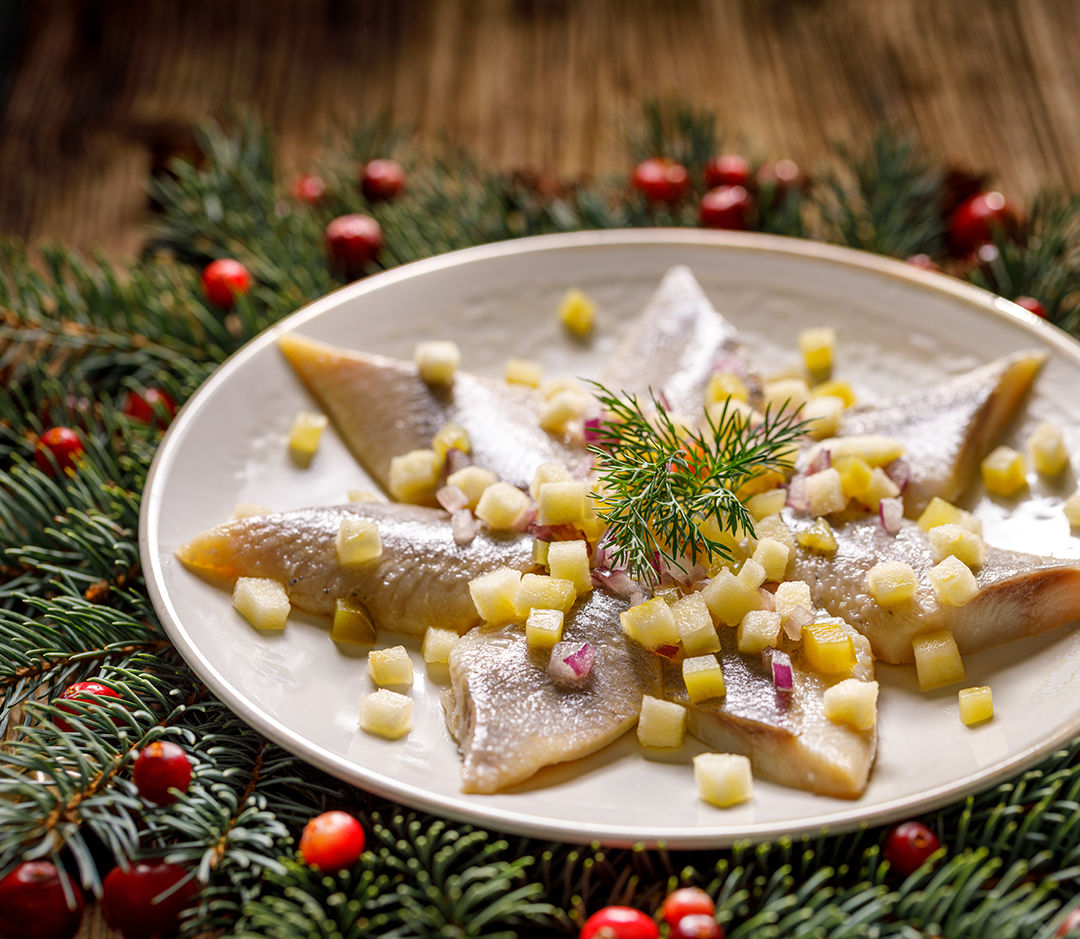 Christmas Herrings fillets with apples, pickled cucumbers, red onion and spices on a ceramic plate on a festive decorated wooden table, close-up. Christmas, traditional dish