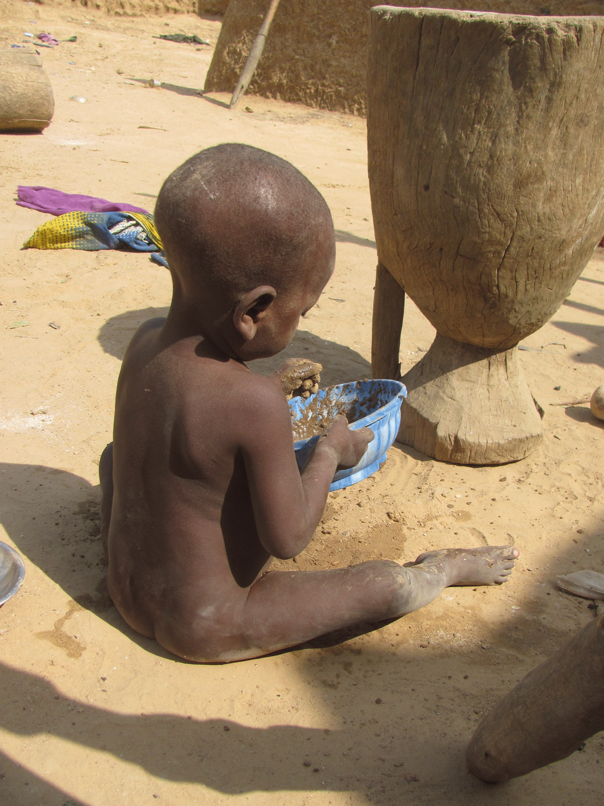 A boy plays with soil on the floor of his home
