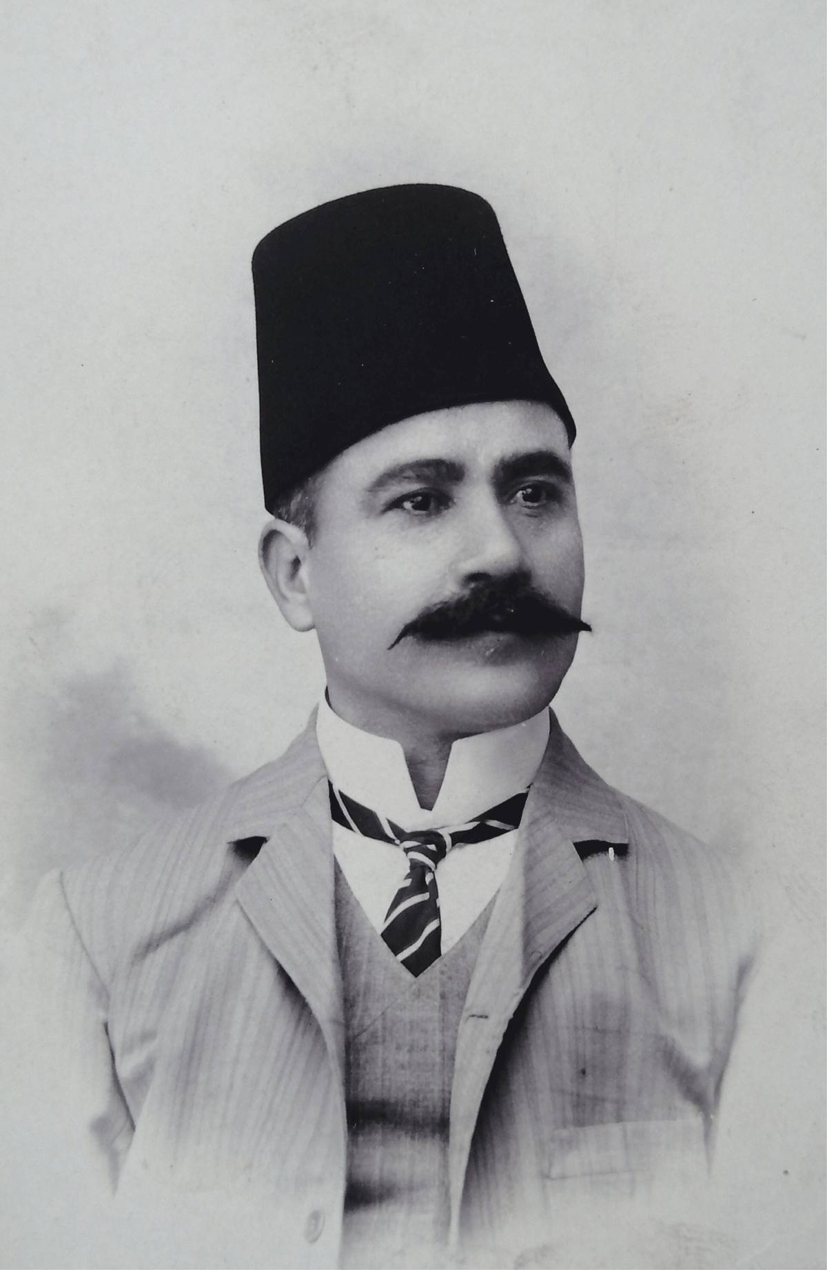 Photographic portrait of Mr Gejou in a three piece suit, a high collar, and a Fez hat