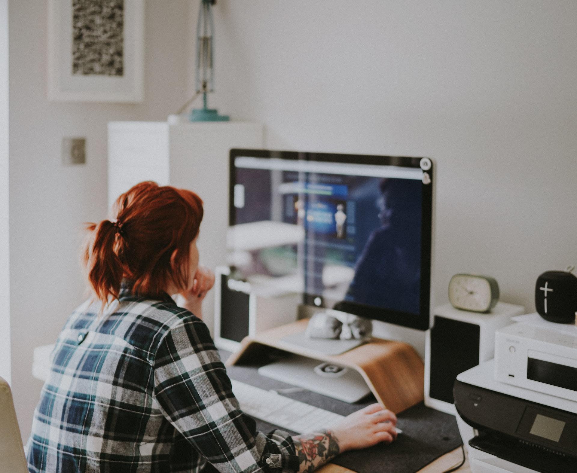 Red-haired woman working on a home desktop computer.