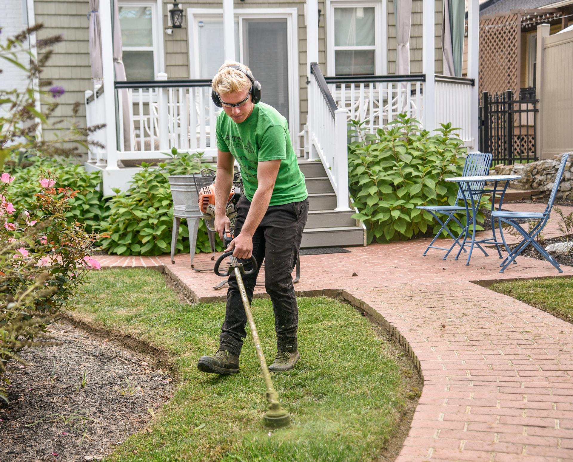 A landscaper using a bushwhacker to trim some grass.