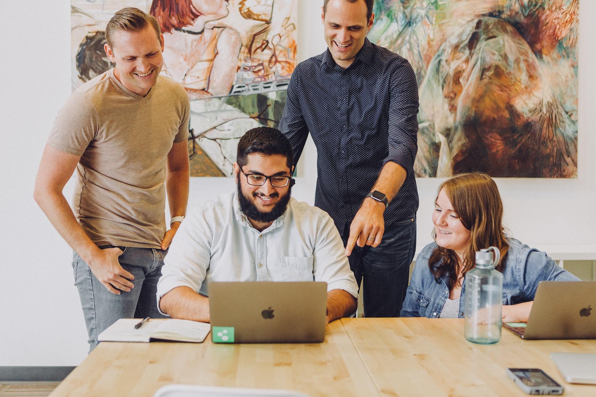 A team huddled around an open laptop computer on a large wooden table.