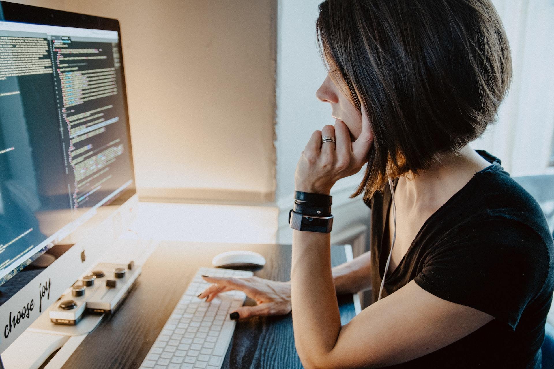 Woman sitting at a desk in front of coding computer screen.