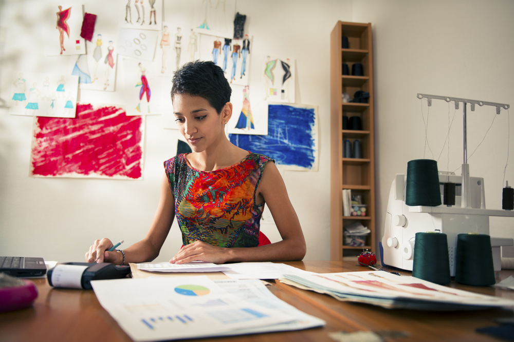 Young hispanic self-employed woman checking bills and doing budget with calculator, computer, and papers.