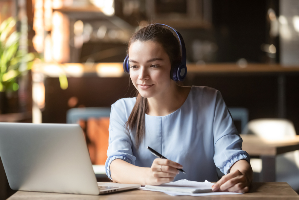 Focused young woman wearing headphones using laptop in cafe.