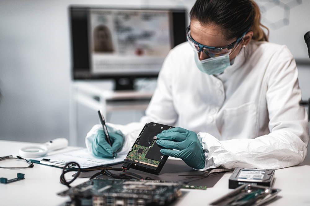 Forensic science in white lab coat examining computer hard drive.