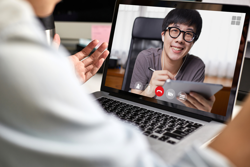 Young Asian man on the screen taking notes during a video call at home.