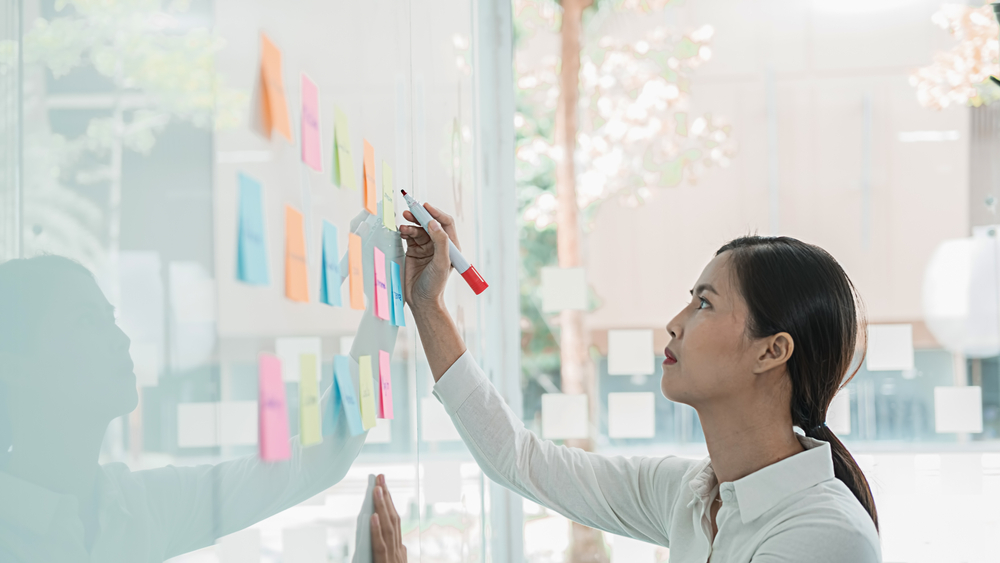 Woman works on a white board with sticky notes during a nonprofit meeting.