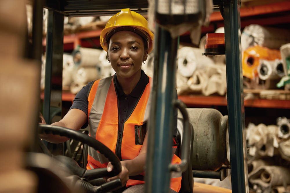 Portrait of a young female forklift operator moving boxes around a textile warehouse.