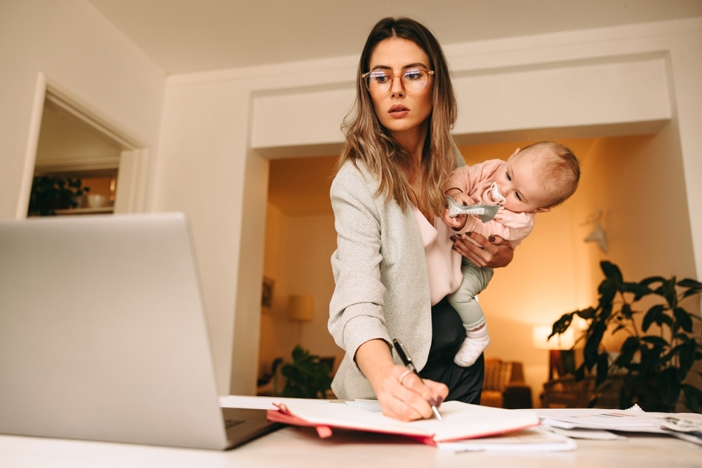 Design professional making notes while holding her baby.