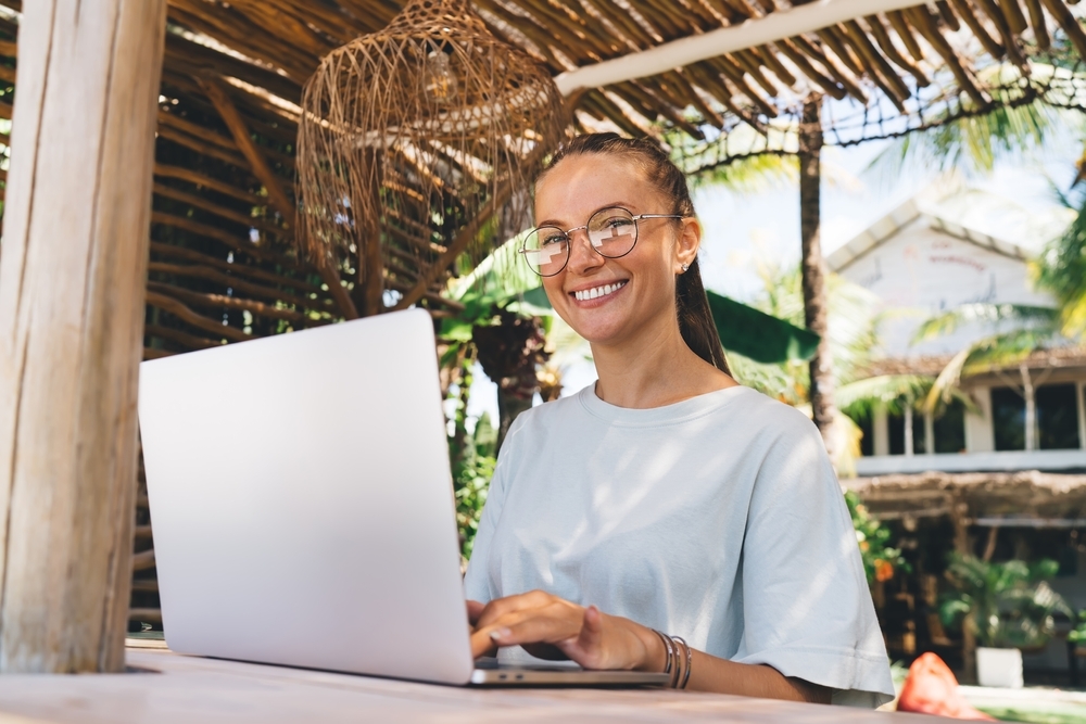 Portrait of happy female worker wearing eyeglasses using computer during remote working outdoors.