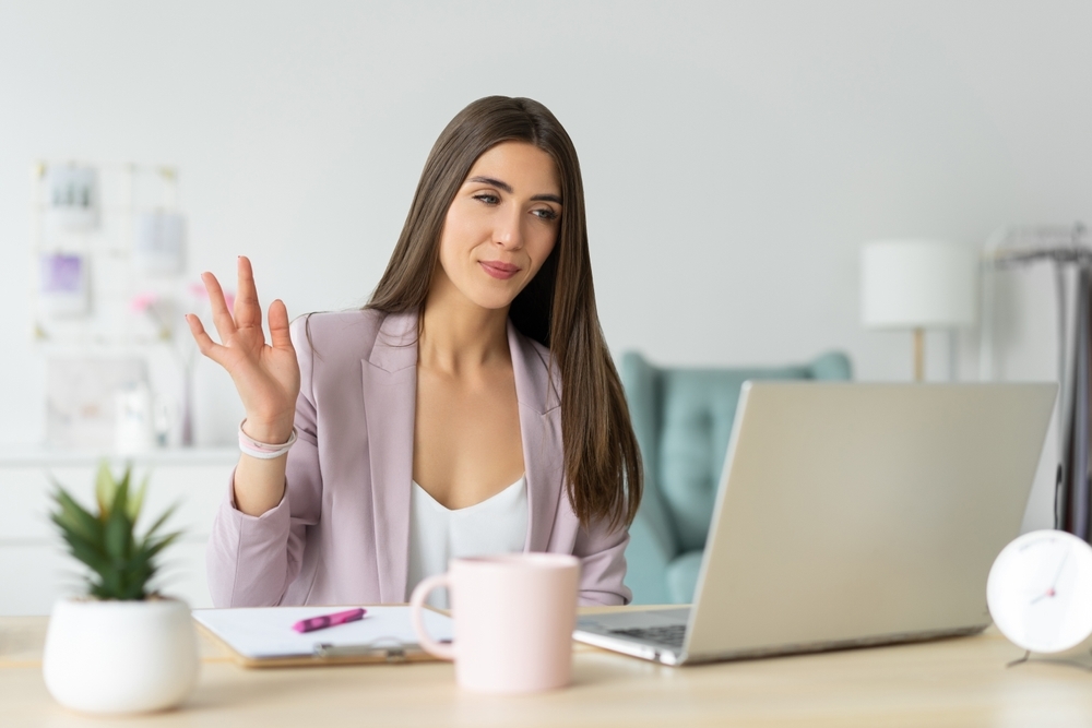 Woman greeting a client over a computer.