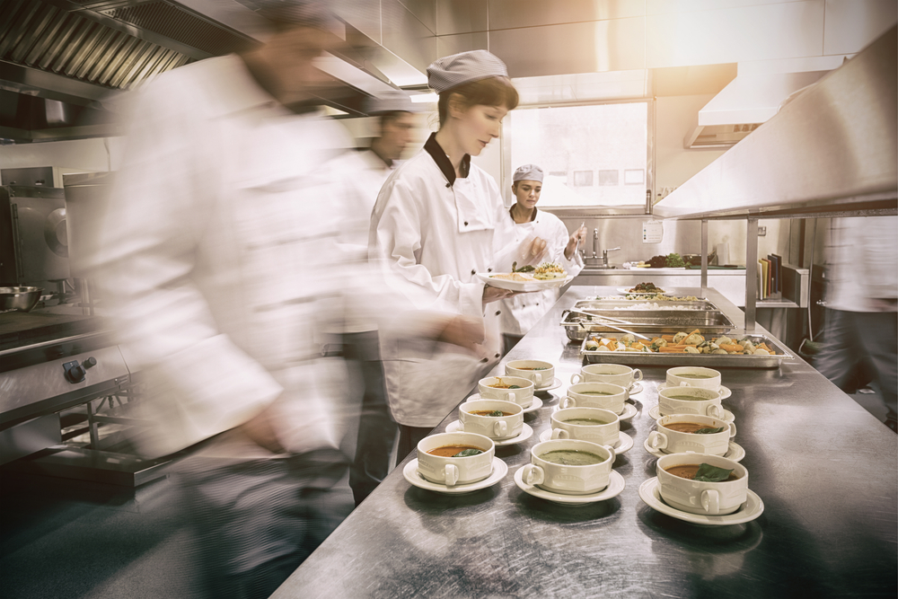 Four chefs working in a modern kitchen preparing soups and dishes.