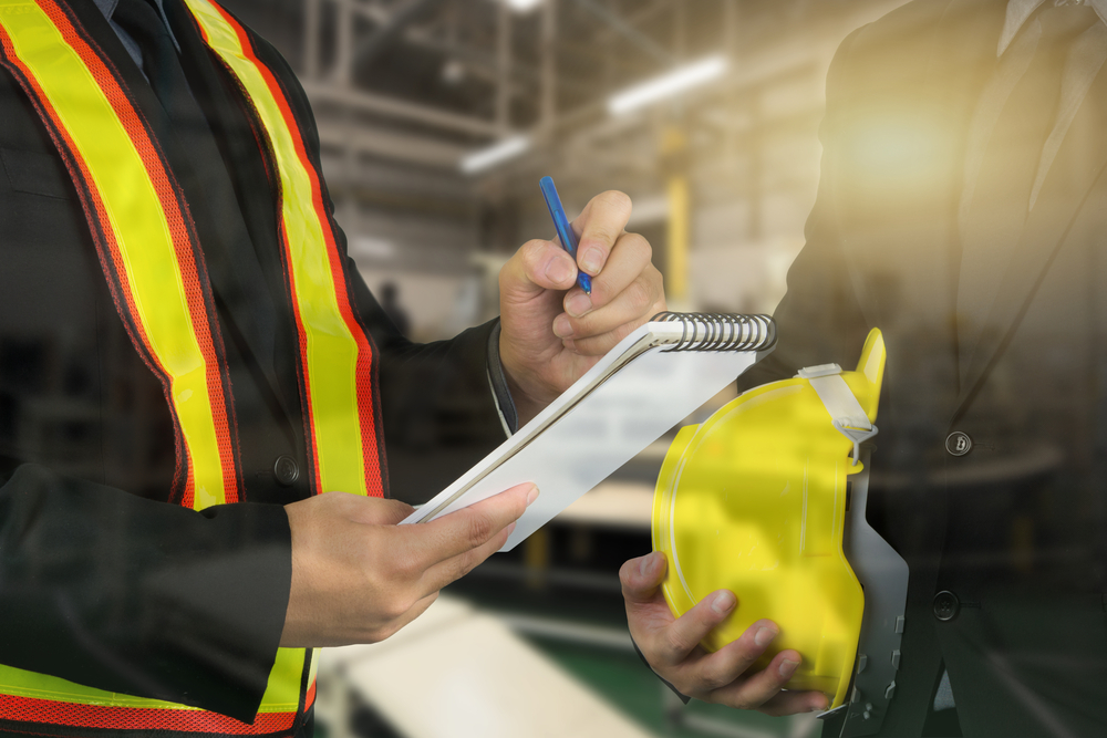 An occupational health and safety officer talking to a man in a factory setting while doing an inspection.