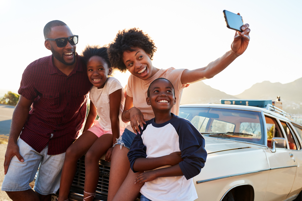 Young family on a roadtrip together taking a picture beside their car.