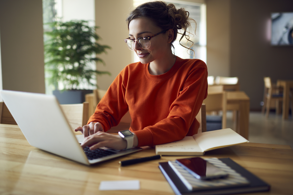 Professional young female copywriter in trendy eyewear typing on a laptop computer.