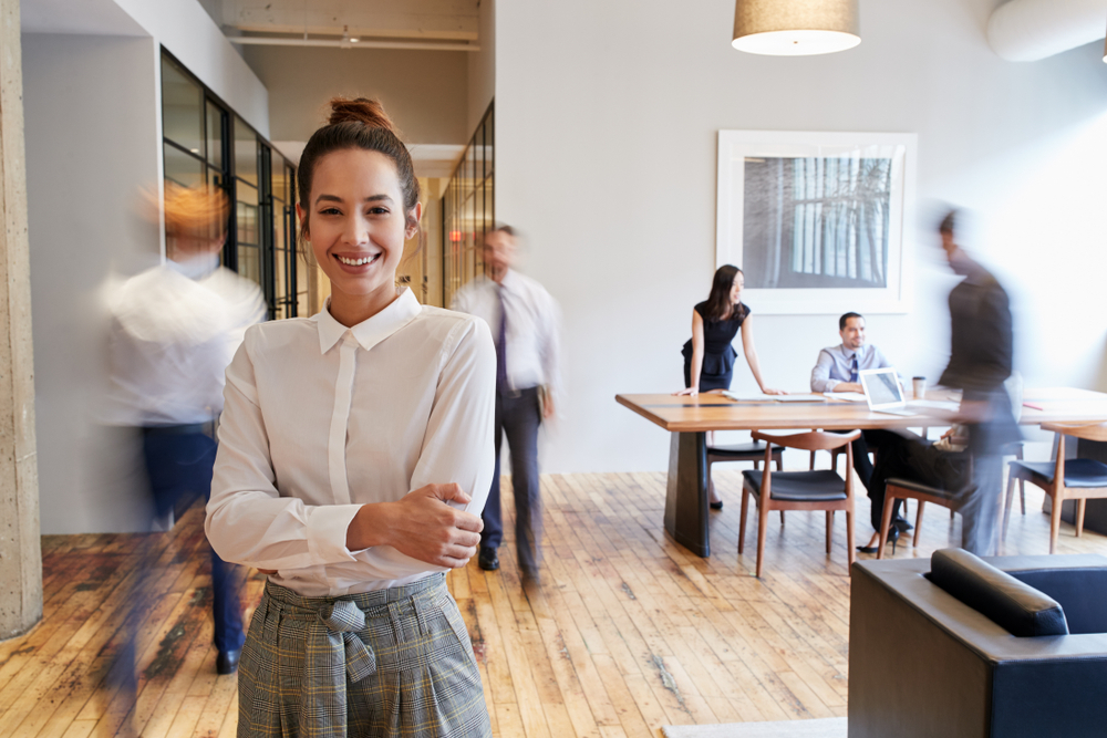 Portrait of young woman in a busy modern workplace.