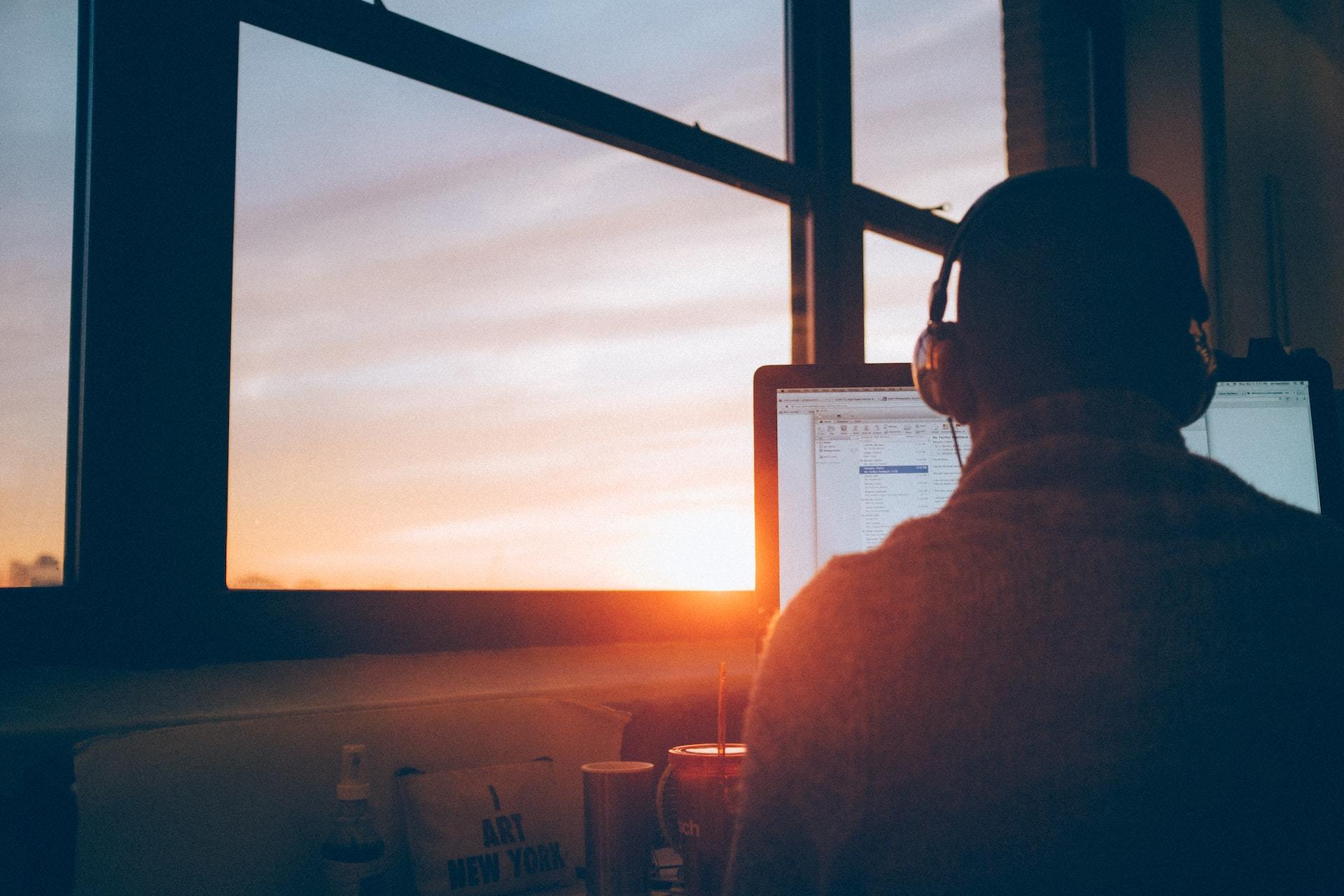 The sun setting on a guy working at his desk at home.