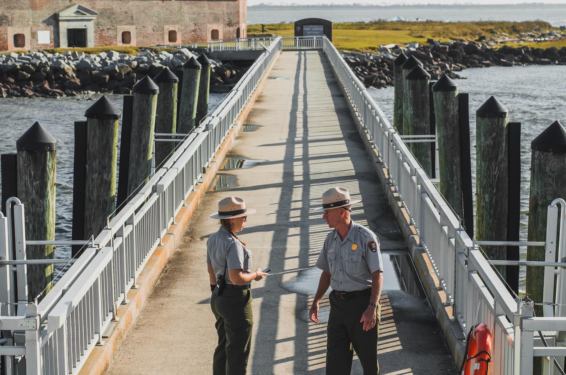 Two park rangers talk at the end of a long concrete pier.