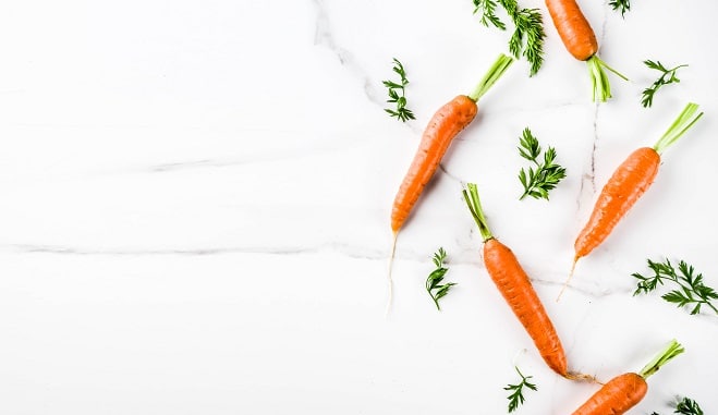 Fresh raw carrots with green leaves, white marble background copy space top view