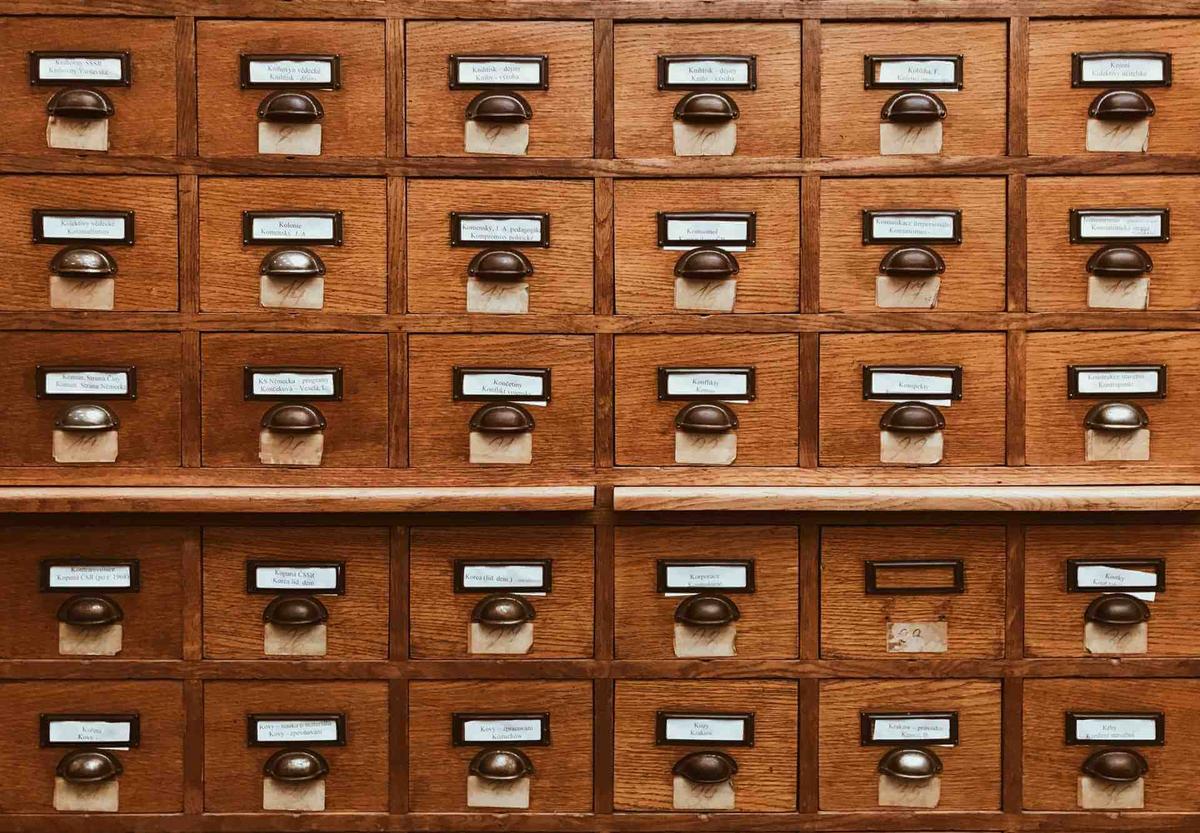 Brown, wooden filing cabinet with many labelled drawers, representing how to organize email with a detailed filing system