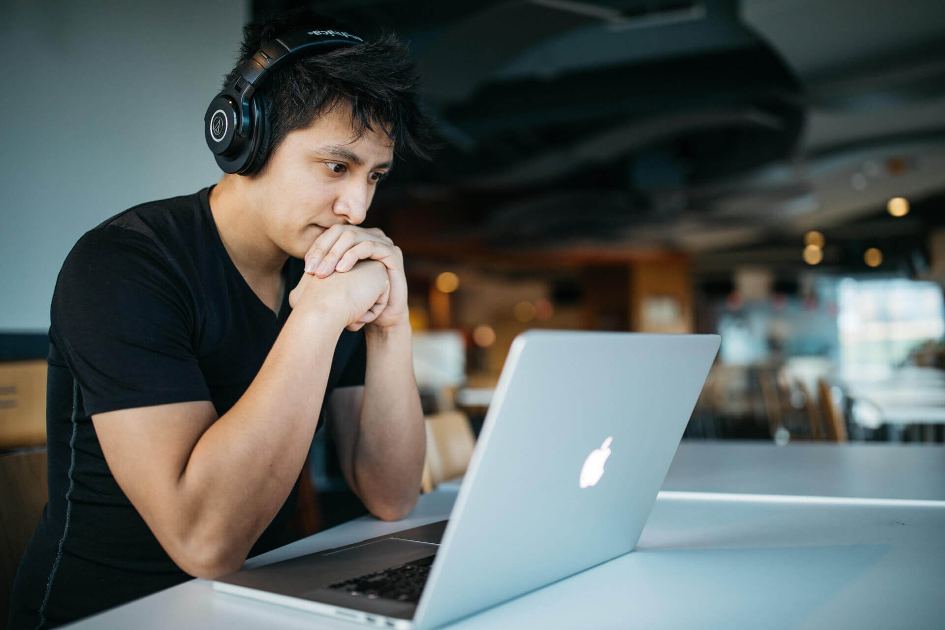 young man wearing headphones sitting in front of macbook in busy room focusing with binaural beats