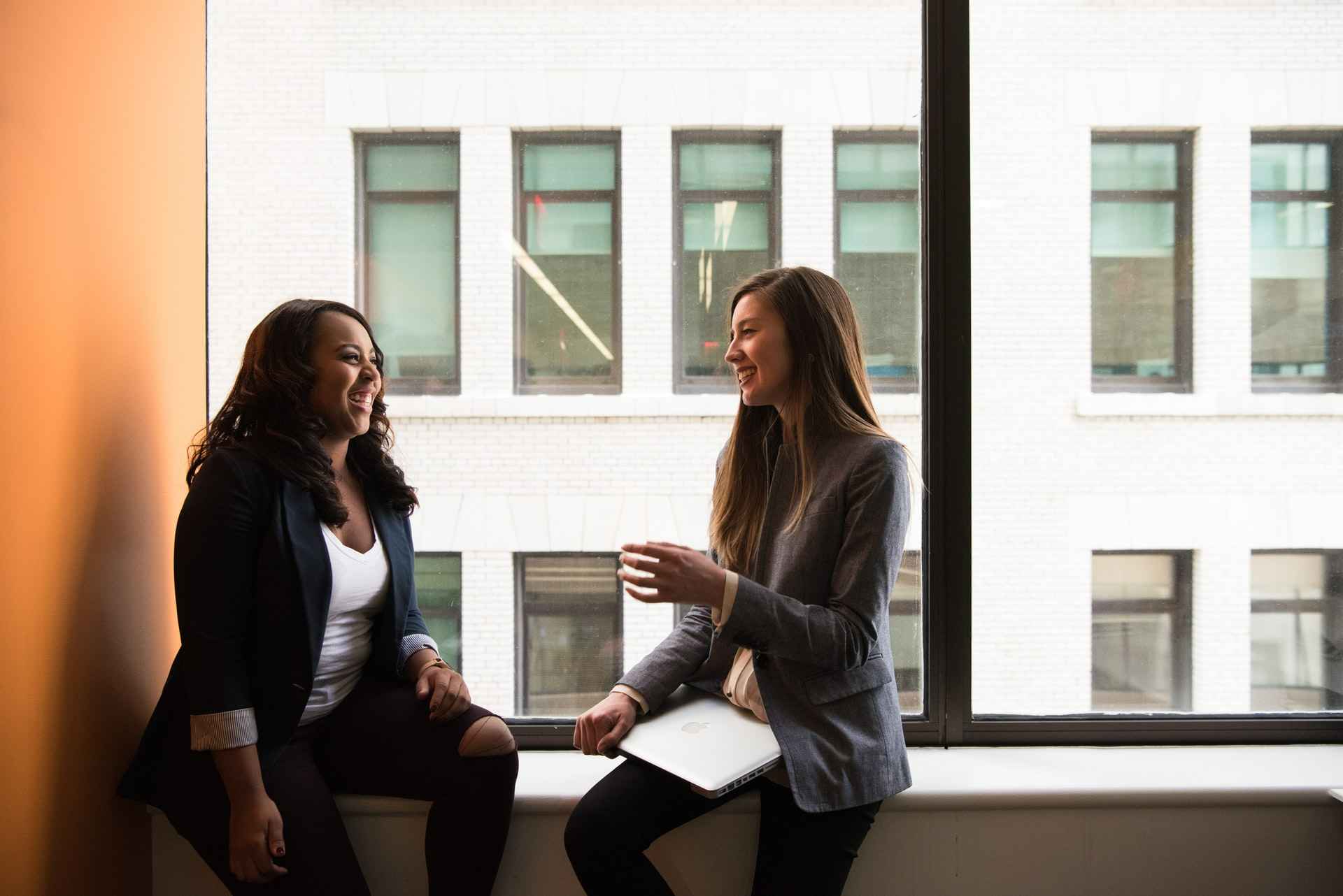 Two women sitting on a window sill in the office talking about the Big Quit