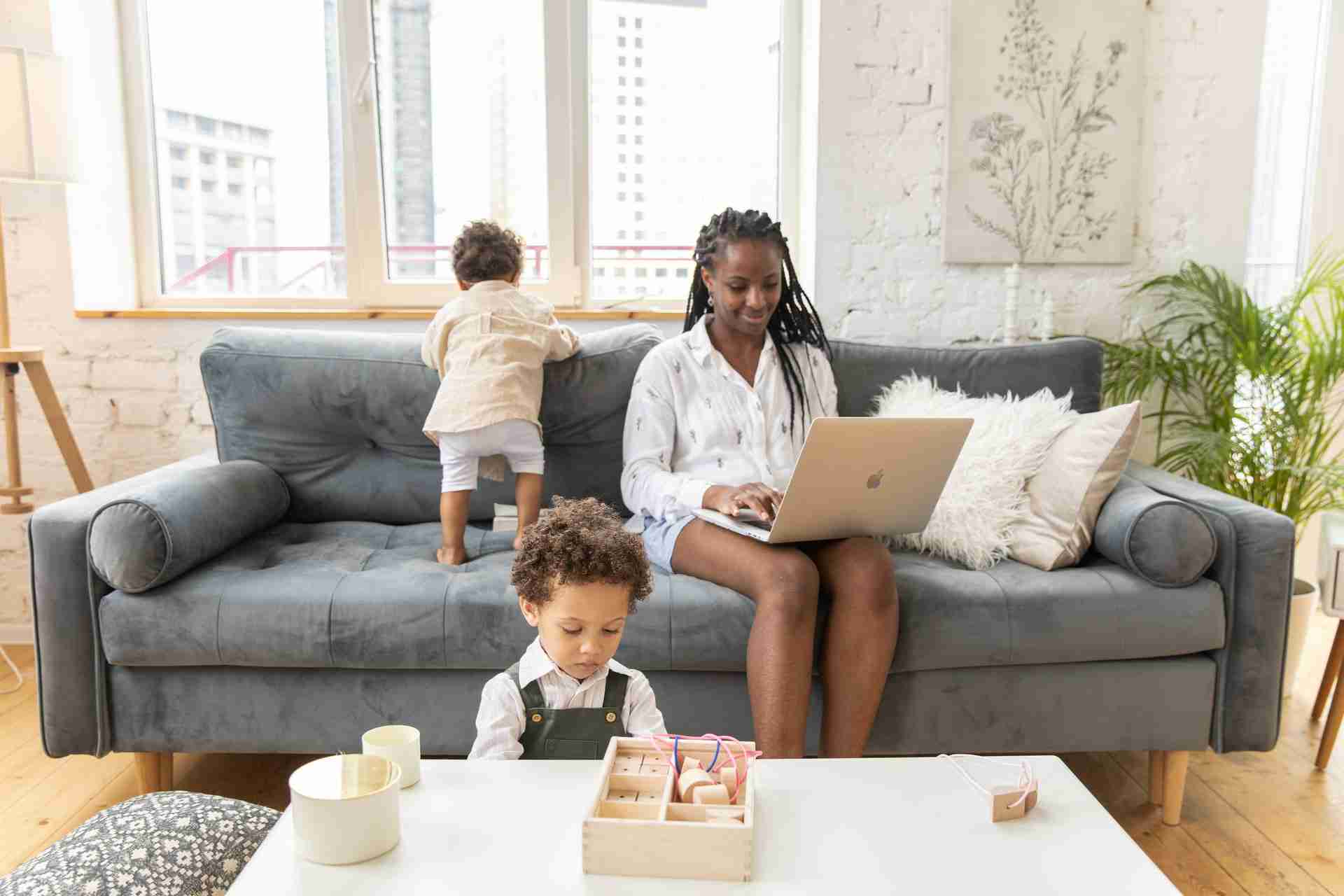 Working mother sitting at home with her two children while working on her laptop