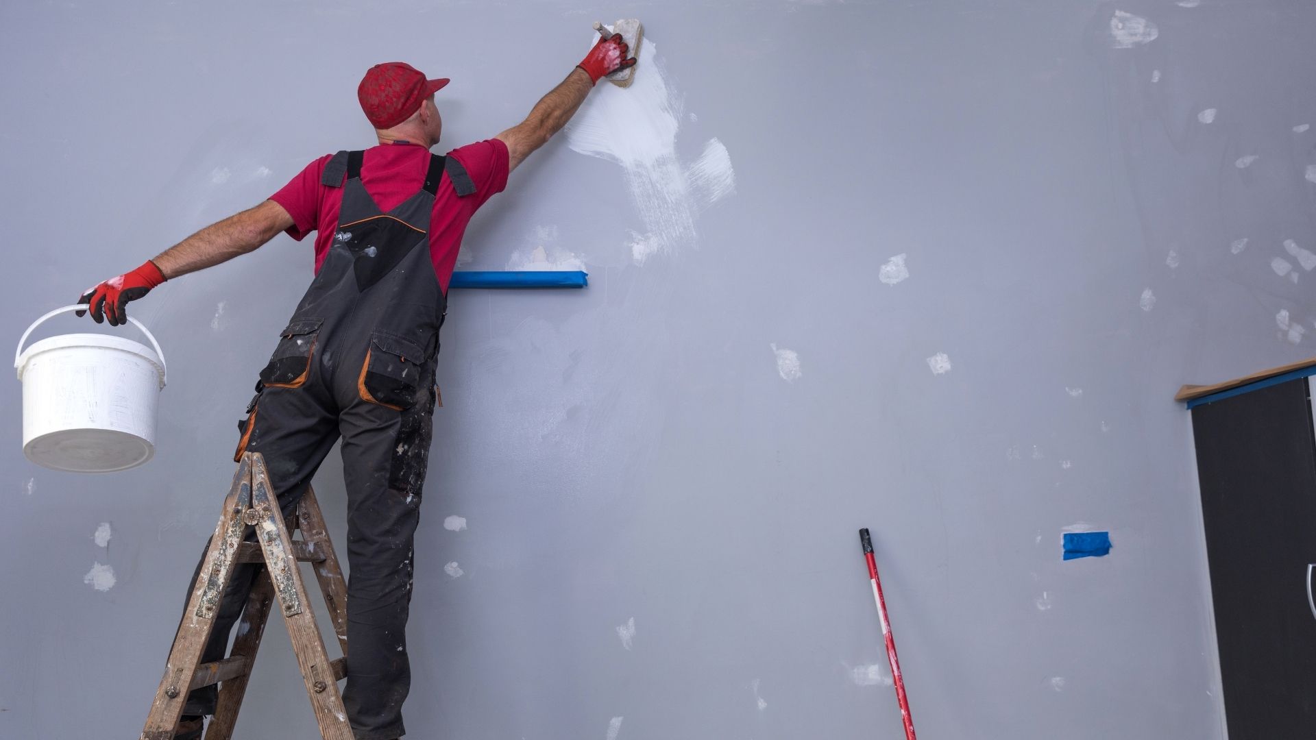 Szobafestő létrán állva, faljavítás közben