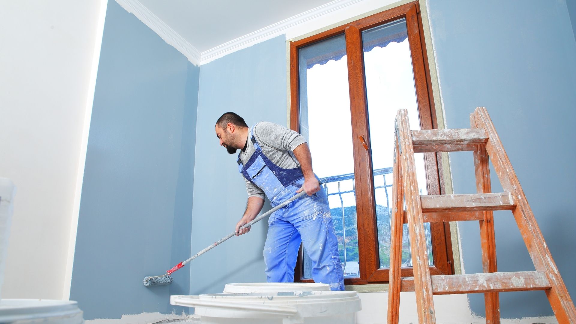 Szobafestő munka közben világoskékre hengerel egy falat