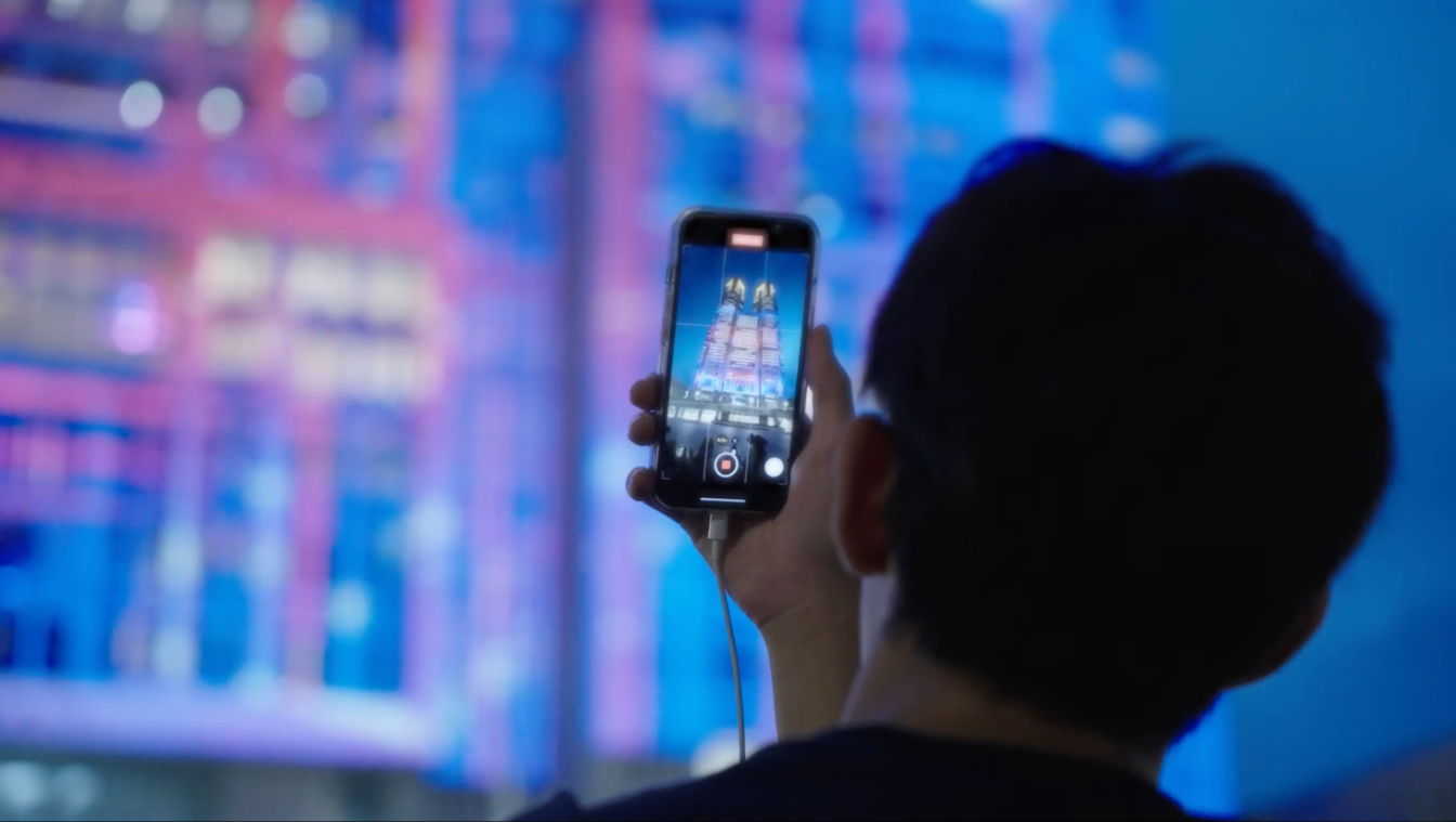 A visitor uses a smartphone to take a picture of the illuminated Tokyo Metropolitan Government Building.